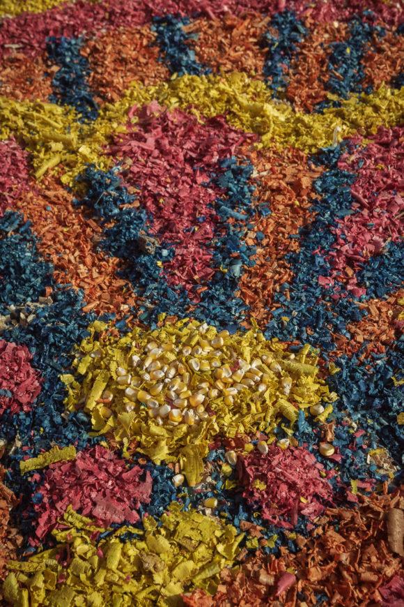 Corn kernels form the circle of the sun in this sawdust carpet on the floor of an altar.