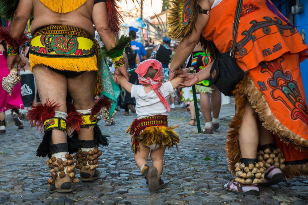Parents help an even younger Aztec dancer take part in the procession.