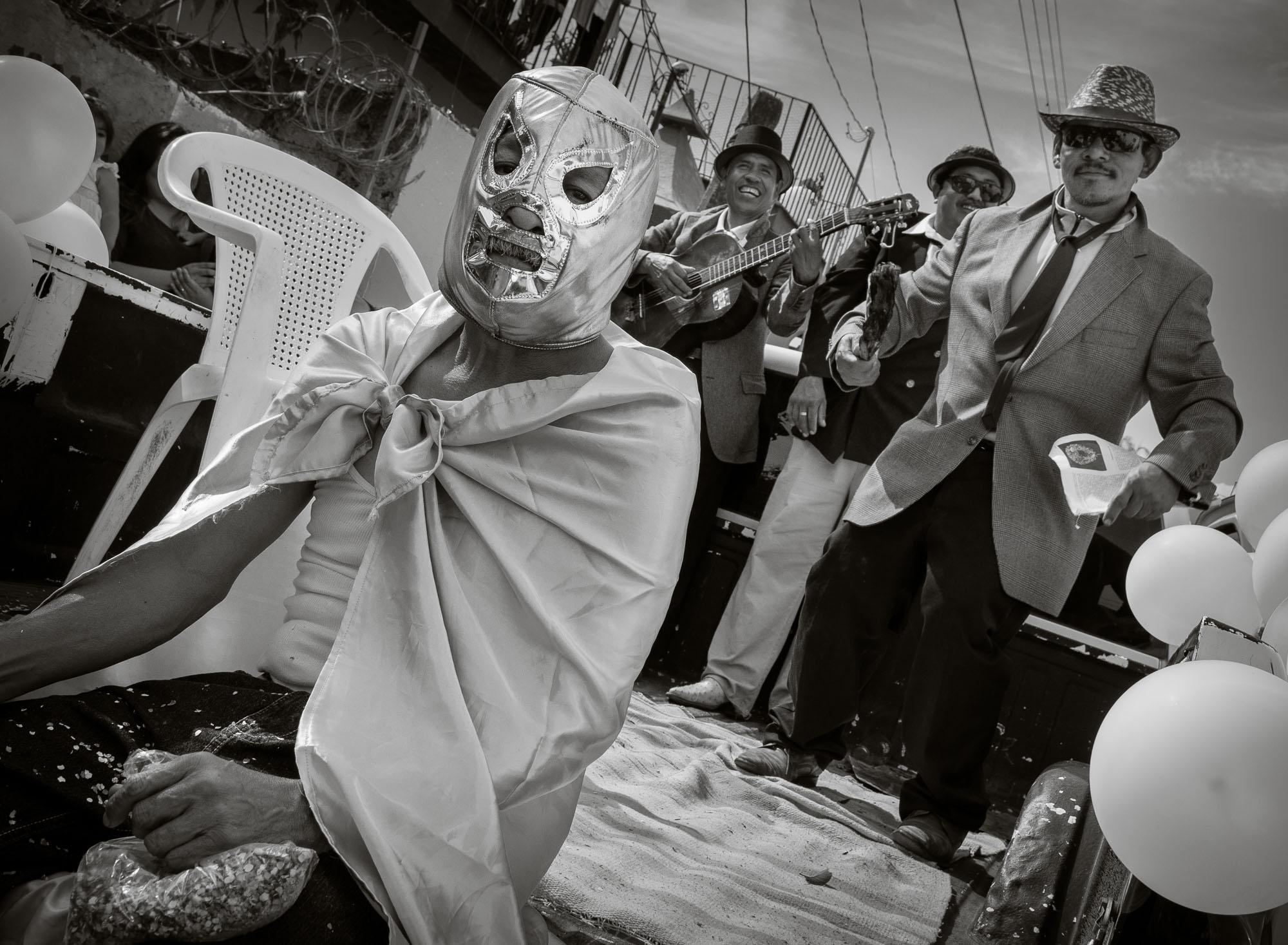 A man wearing a Mexican lucha libre mask sits on the tailgate of a truck as musicians play along to pre-recorded hip hop music during the 2015 New Year's Day Parade in Ajijic, Jalisco, Mexico