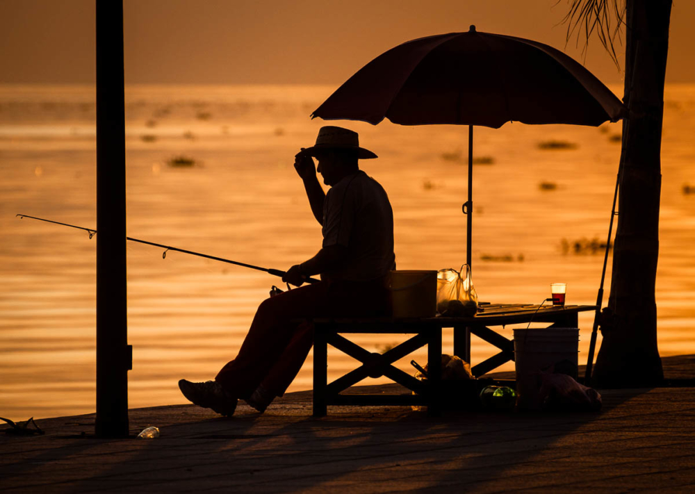 A man adjusts his hat while fishing in the evening on Lake Chapala from the Ajijic malecón (boardwalk).