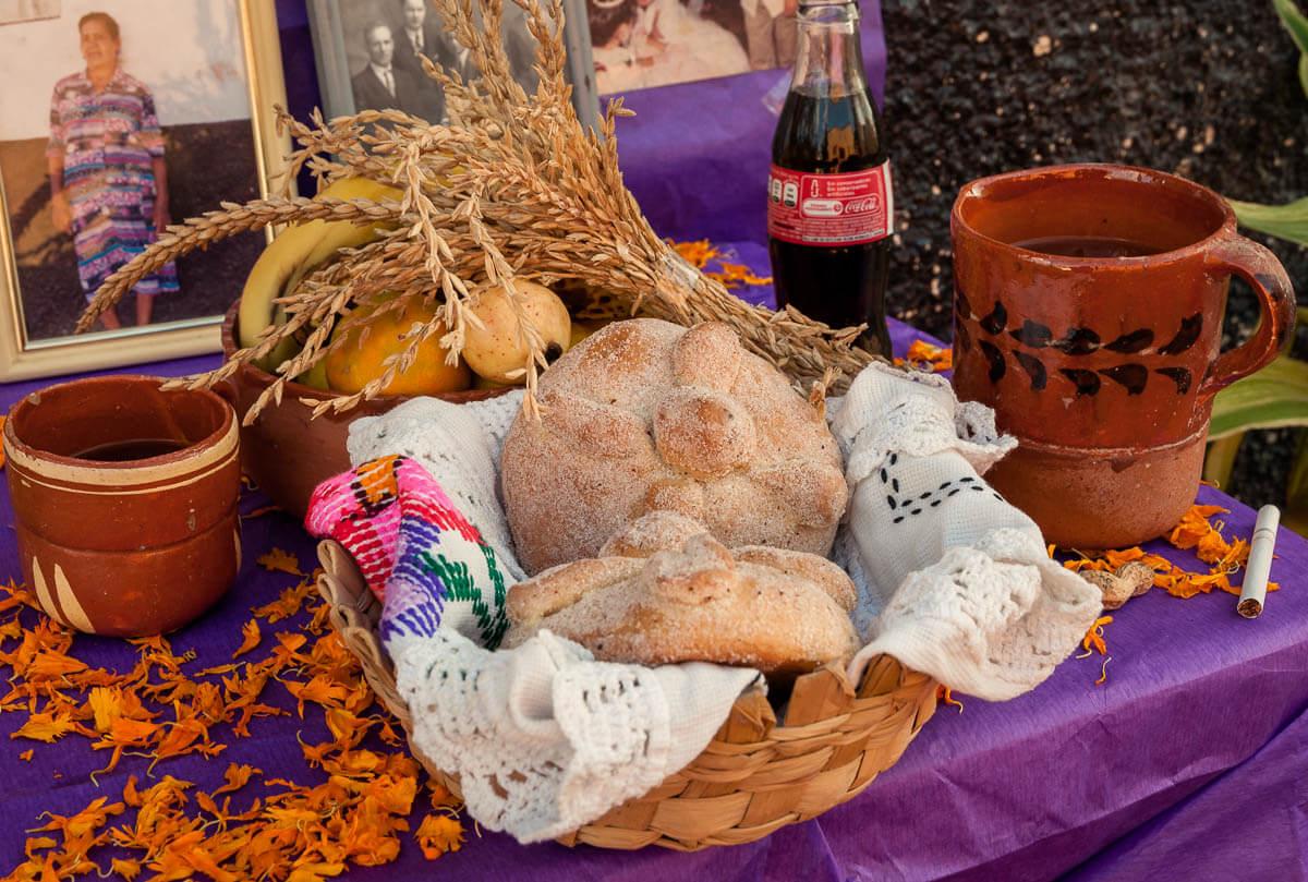 Pan de muertos, bread of the dead, is offered on an altar along with grains, fruits, beverages, marigolds, fruits and a cigarette.