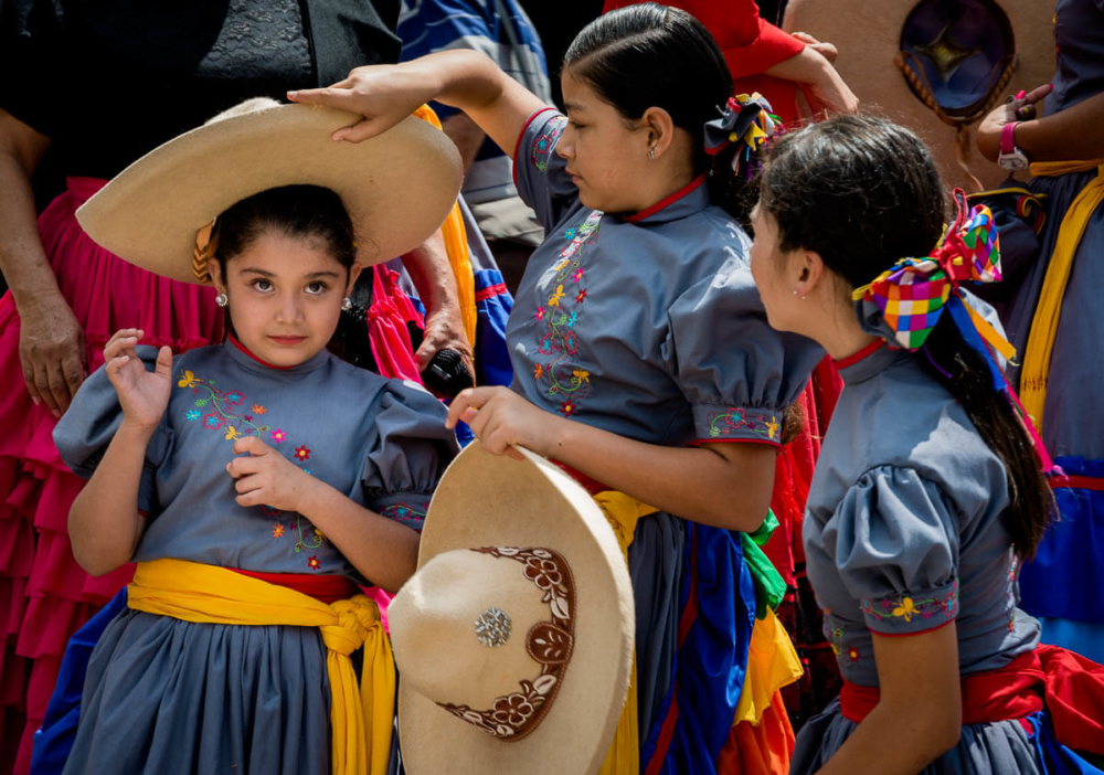 Escaramuza cowgirls helping each other put on their sombreros.