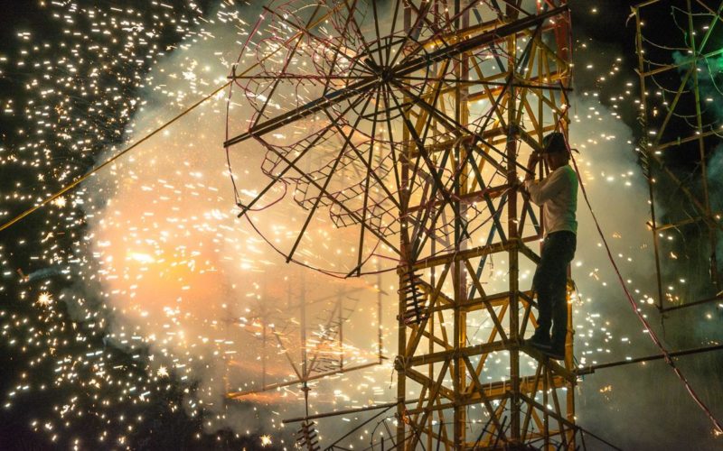 A man oversees the lighting of one of the parts of a large fireworks castle.
