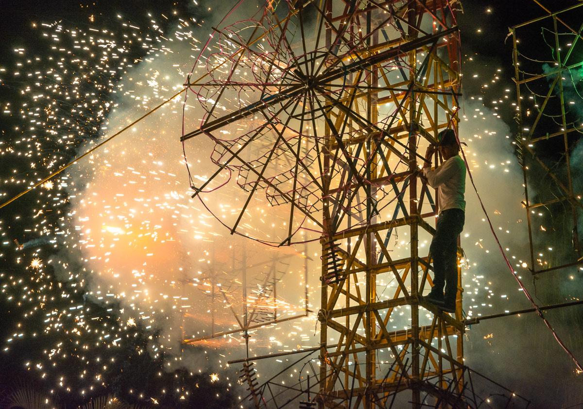 A man oversees the lighting of one of the parts of a large fireworks castle.